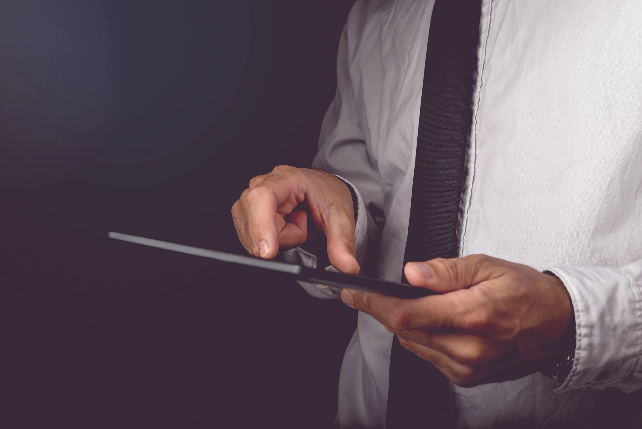 Businessman in a white shirt and dark tie using a tablet device in a modern office