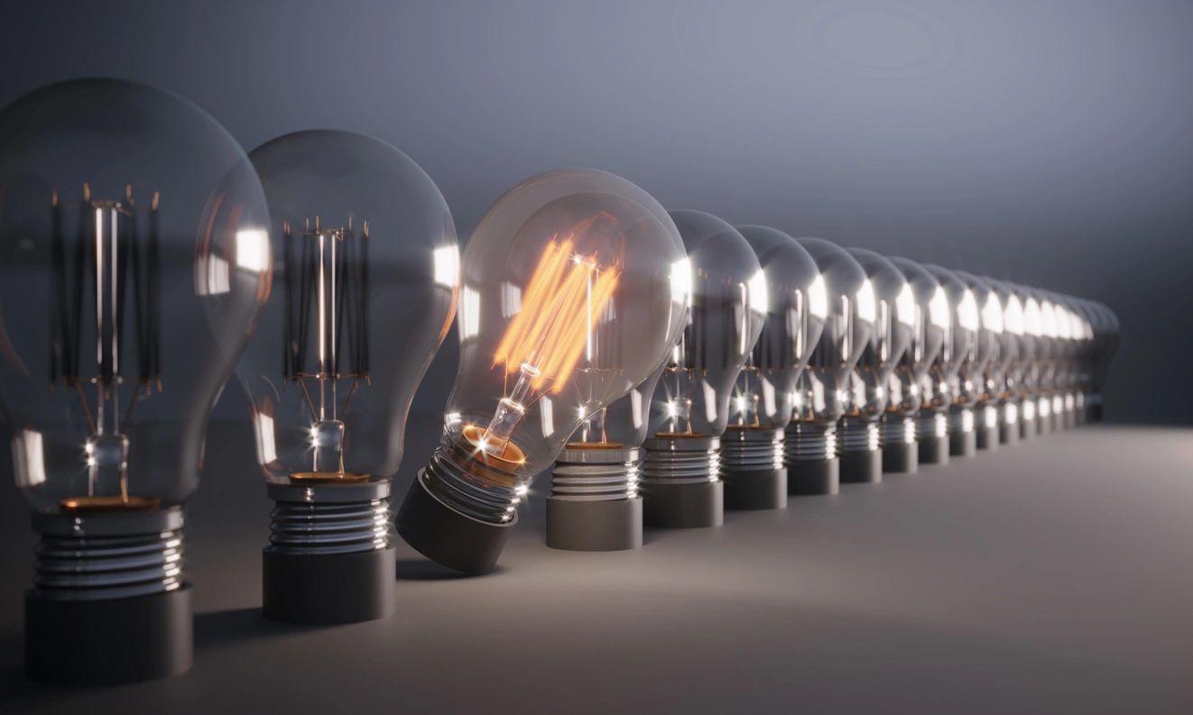 Row of Edison filament bulbs, one glowing brightly among unlit bulbs — the idea that stands out