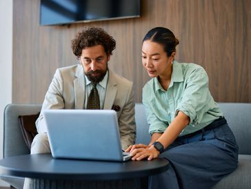A man and woman collaborating on a laptop on a sofa in a modern office