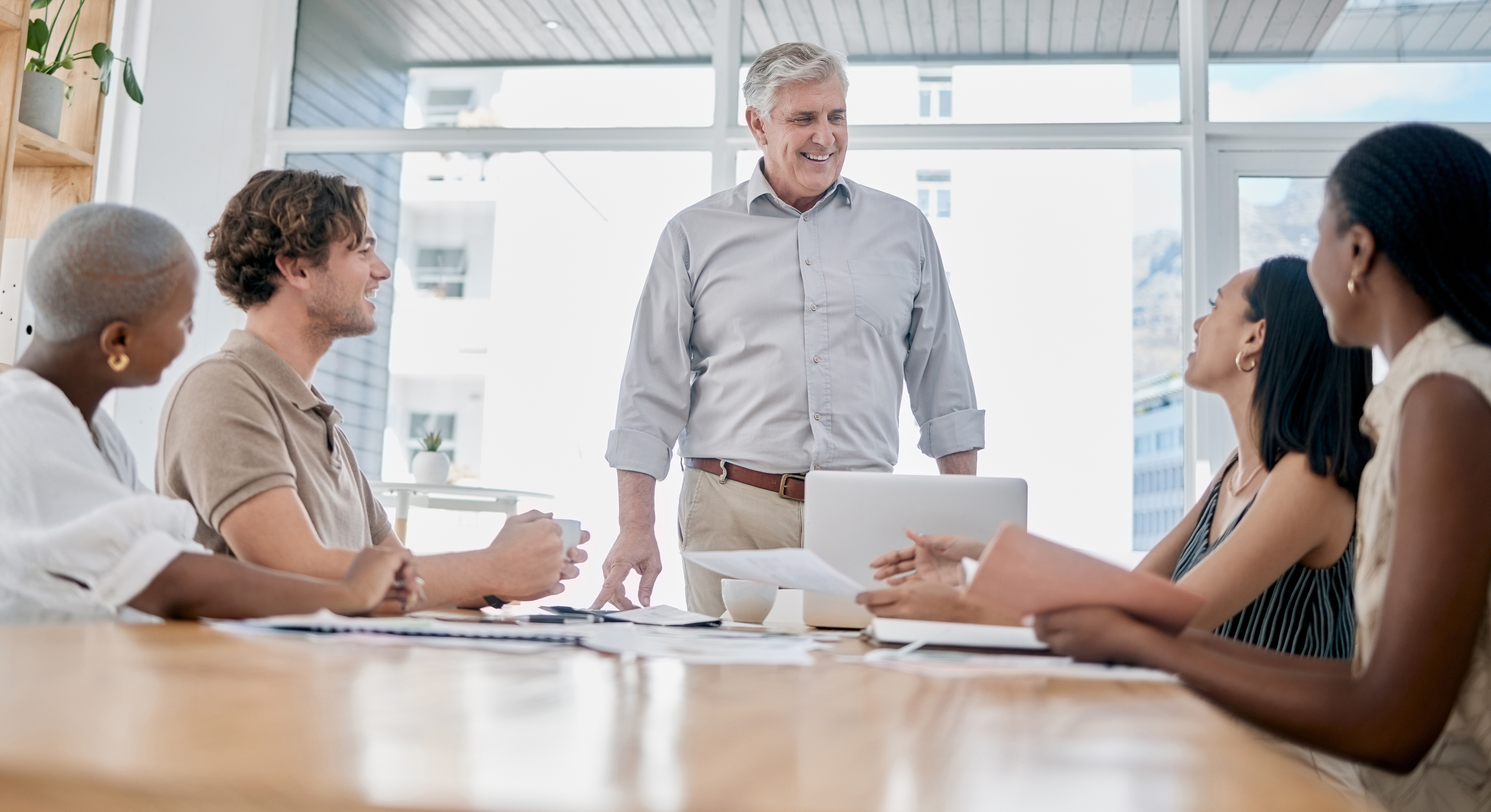 A leader standing at the head of a bright conference table leading a team working session