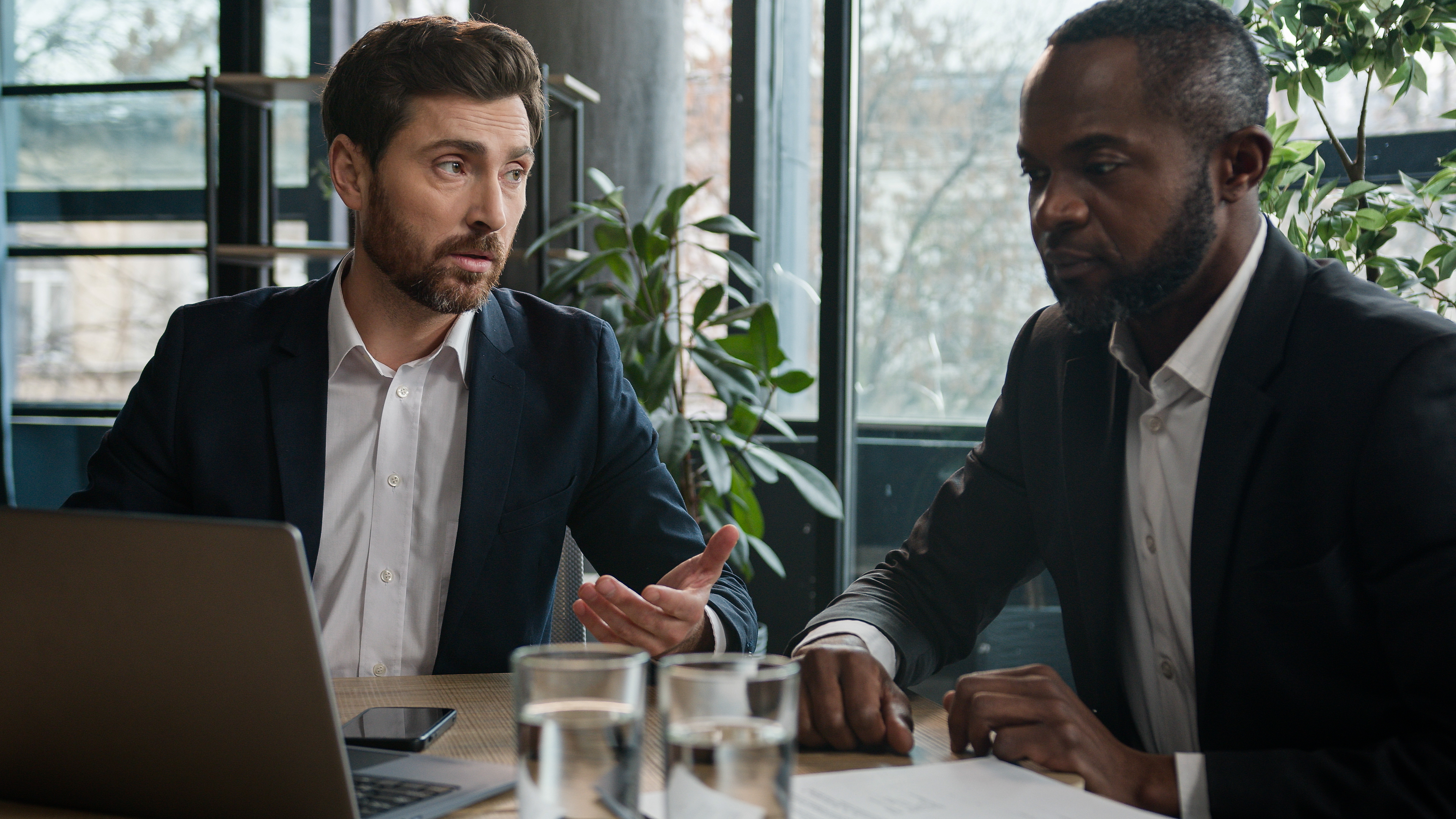 Two executives in conversation across a conference table in a light-filled office